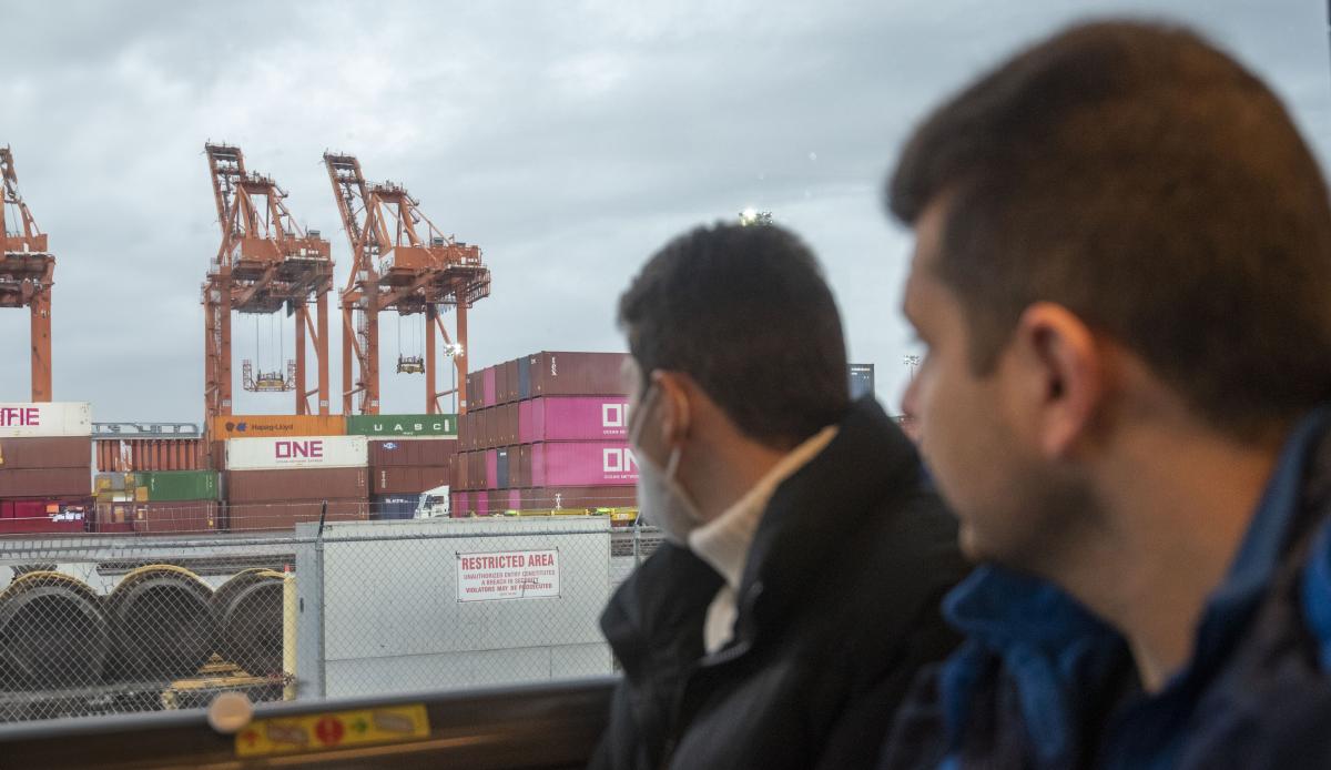 Two men looking out a bus window at some cranes. 