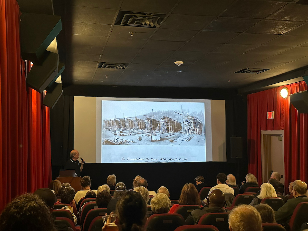 A man holding a microphone giving a presentation to a theater audience.