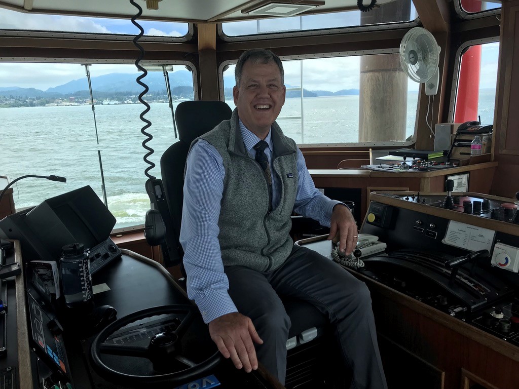 A man in the captain's seat of a boat sits smiling. 