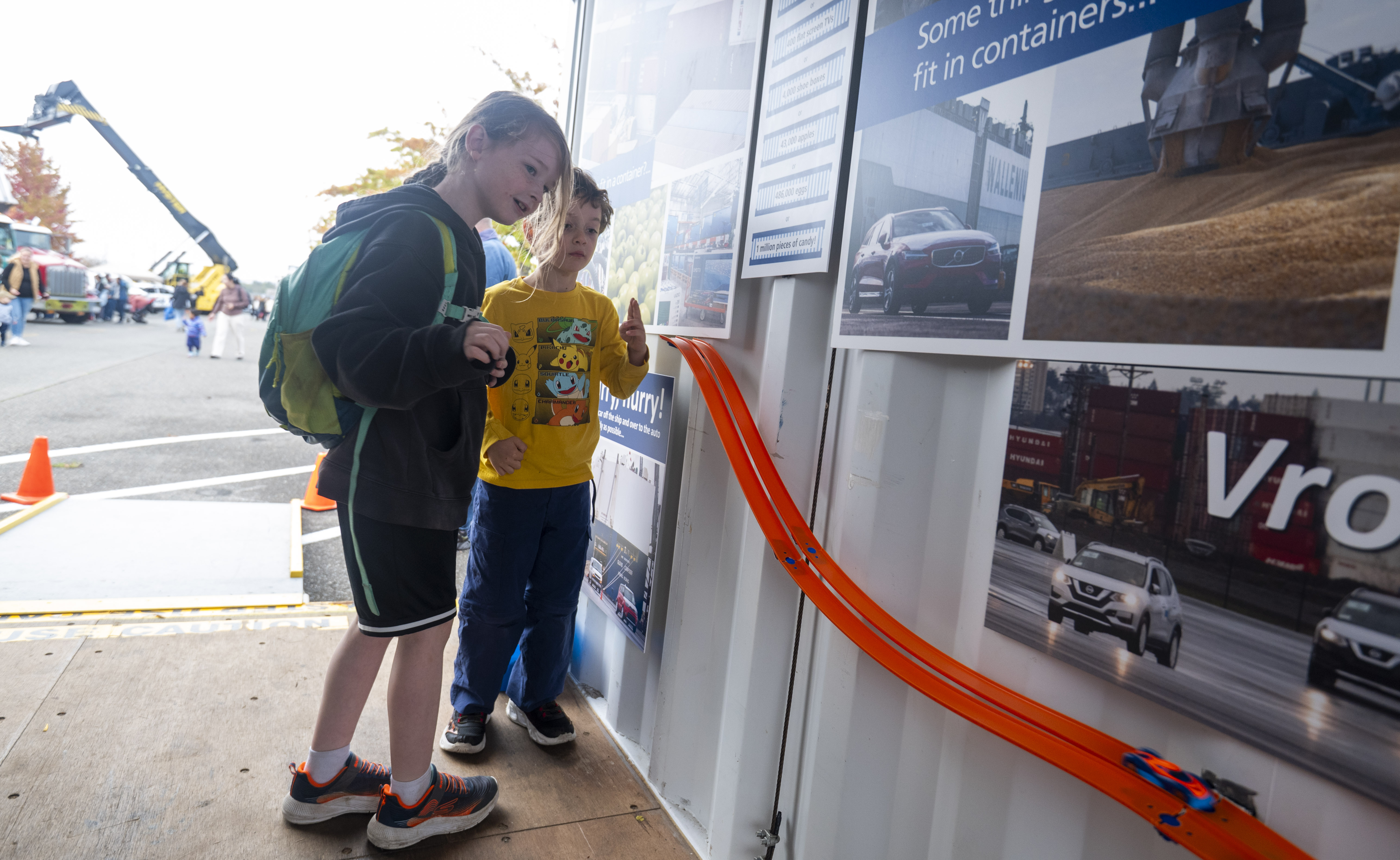 Two children play with a toy car on an orange track attached to a wall.