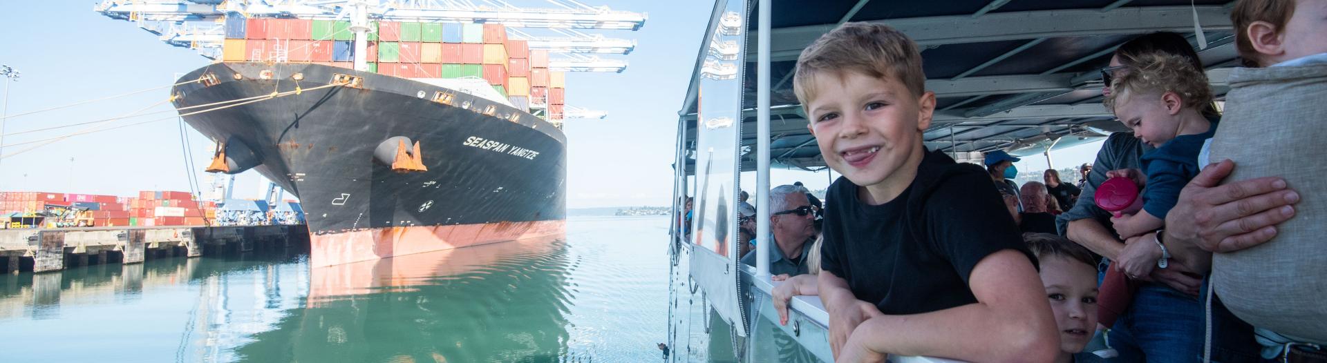 A young boy leans over the railing of a boat while grinning.