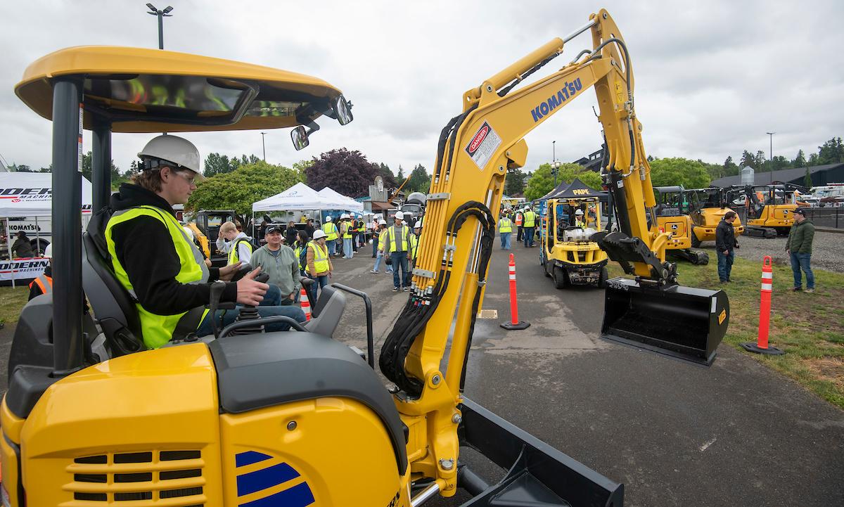 A student in protective gear sits in the cab of an excavator.