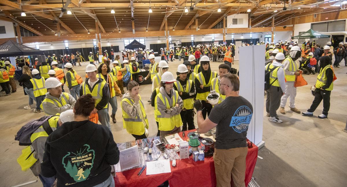 Two adults demonstrate wiring to a group of students at a career fair.
