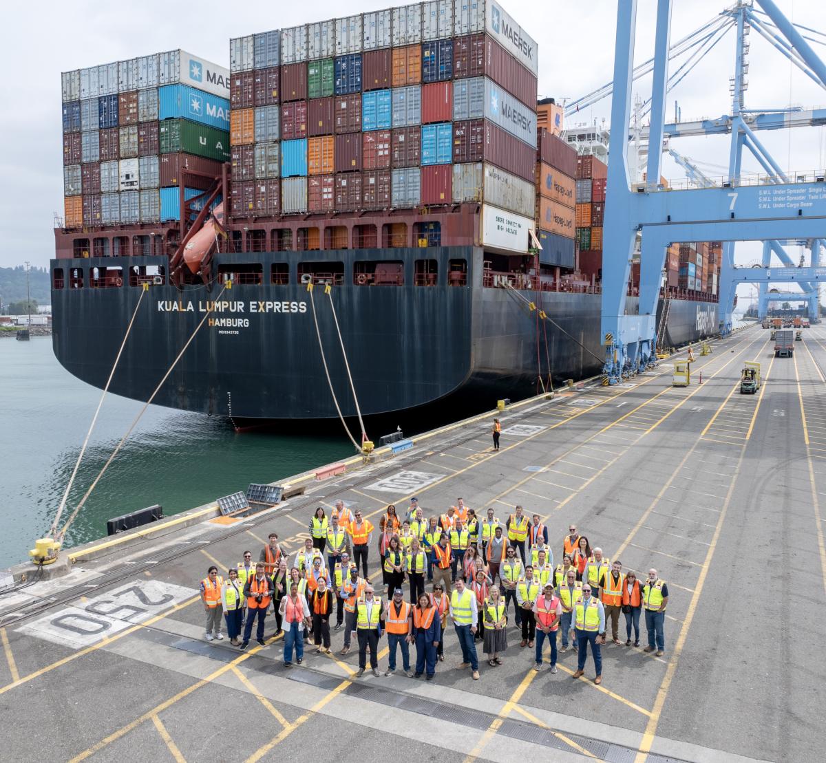 Aerial shot of a group of people standing on a port terminal in front of a container ship.