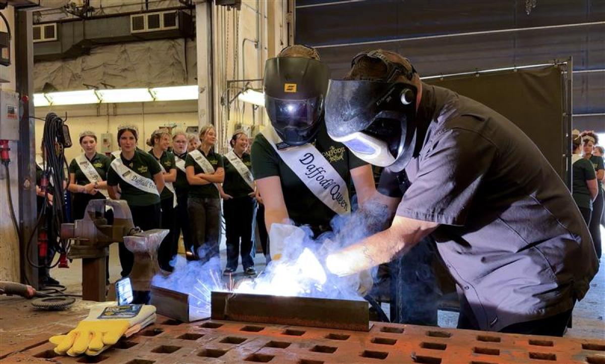 A port employee helps a young woman in a Daffodil Festival sash weld in a maintenance shop.