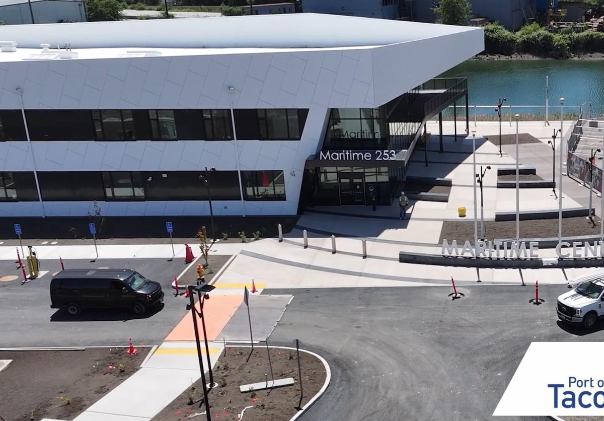A modern white building and parking lot with two vehicles in front.